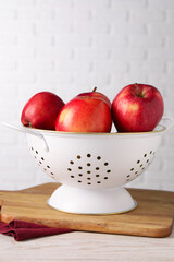 Fresh apples in colander on white wooden table