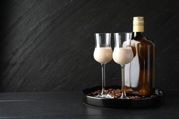 Coffee cream liqueur in glasses, bottle and beans on black wooden table, space for text