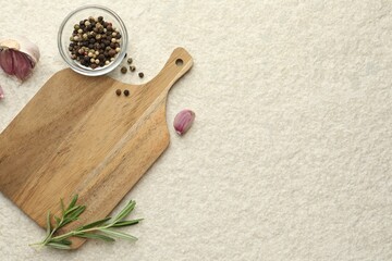 Cutting board, garlic, pepper and rosemary on white textured table, flat lay. Space for text