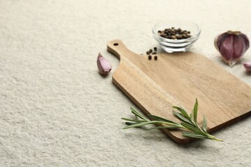 Cutting board, garlic, pepper and rosemary on white textured table. Space for text