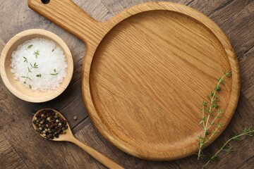 Cutting board and different spices on wooden table, flat lay