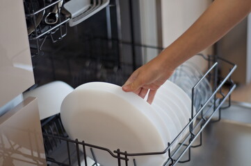 kids hand putting white plate in dishwasher, close up