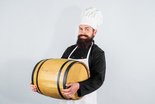 Male brewer in apron holding barrel with craft beer at brewery factory. Bearded man in chef hat and uniform with wooden keg. Traditional German beer festival. Oktoberfest celebration. Beer pub or bar.