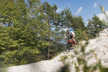 Obraz premium Male electric mountain bike rider going downhill and braking on a hilly rocky trail, low-angle shot. E-mountain biking concept.