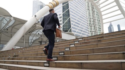 Smart caucasian businessman walking up stairs surrounded by urban view. Side view of ambitious...
