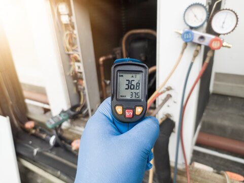 Professional engineer wearing blue gloves using thermo gun for temperature check on the hvac air cinditioning syatem. Temperature check concept on the compressor, condensor , refrigerant system hvac.