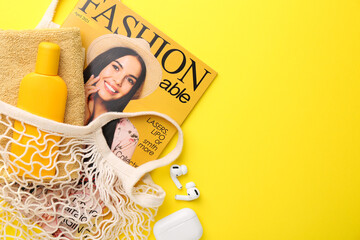 String bag with fashion magazine and beach accessories on yellow background, flat lay. Space for...