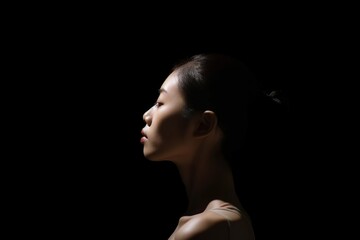 a japanese young woman looks up on isolated black background. a profile of ballerina, her hair pulled into a bun. the concept of hope, mental health, copy space