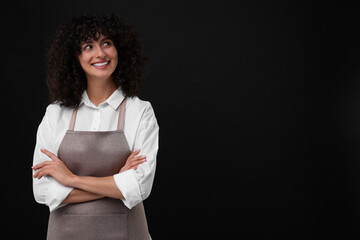 Happy woman wearing kitchen apron on black background, space for text. Mockup for design