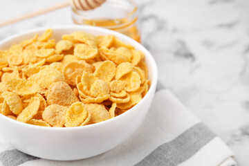 Breakfast cereal. Tasty crispy corn flakes in bowl on white marble table, closeup. Space for text