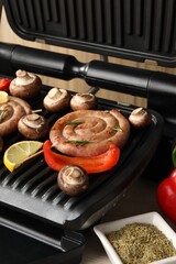 Electric grill with homemade sausages, mushrooms and bell pepper on table, closeup