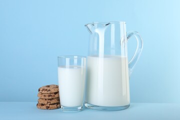 Jug of fresh milk, glass and cookies on light blue background