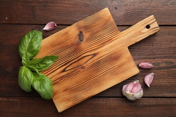 Cutting board, basil and garlic on wooden table, flat lay. Space for text