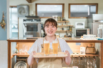 グラスの生ビールを持つ居酒屋・飲食店・カフェスタッフ・ホールスタッフ・アルバイトの若い女性
