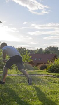 Mature man in white t-shirt enjoys happy news jumping and making turn handsprings on cottage lawn. Funny leonberger runs trying to find happy owner in backyard Vertical Shot.