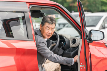 駐車場で自動車のドアを開けてバックする高齢者ドライバーの男性
