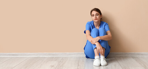 Sad female medical intern sitting near beige wall