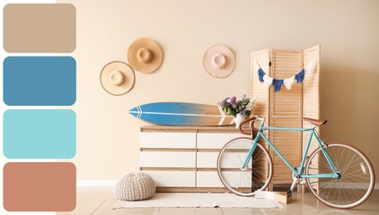 Surfboard on light chest of drawers, folding screen and bicycle near beige wall in room. Different...