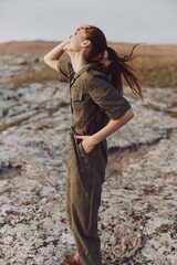 Woman in green jumpsuit standing on rocky hill with hair blowing in wind beauty of nature trip...