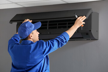 Young electrician repairing air conditioner indoors