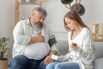 Obraz premium Young woman measuring blood pressure of her father with heart attack at home