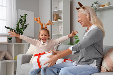 Little girl and her grandmother in reindeer horns with gifts at home on Christmas eve