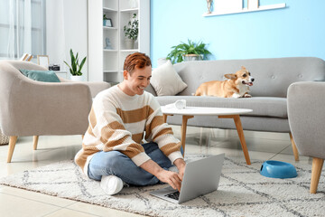 Redhead young happy man with cute Corgi dog and laptop sitting at home