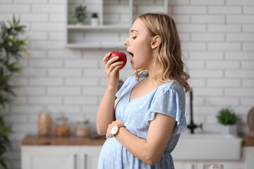 Young pregnant woman eating apple in kitchen