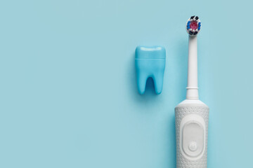 Modern electric toothbrush and tooth model on blue background. World Dentist Day