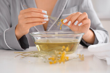 Young woman preparing steam inhalation with herbs at table in kitchen, closeup