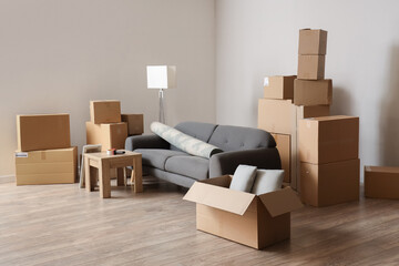 Cardboard boxes with black sofa, rolled carpet and table in living room on moving day