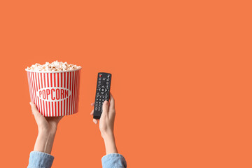 Hands with bucket of popcorn and TV remote on orange background