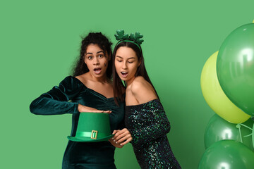 Shocked young women with leprechaun hat and air balloons on green background. St. Patrick's Day...