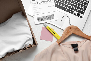 Open parcel with clothes, label and laptop on white table