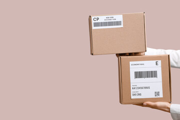 Woman holding cardboard packages with labels and barcodes on pink background