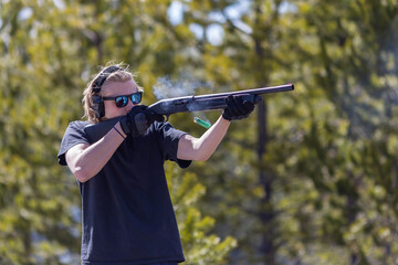 Young man shooting shotgun. Ejected shells flying around.  Gun powder gases from chamber. Side view.