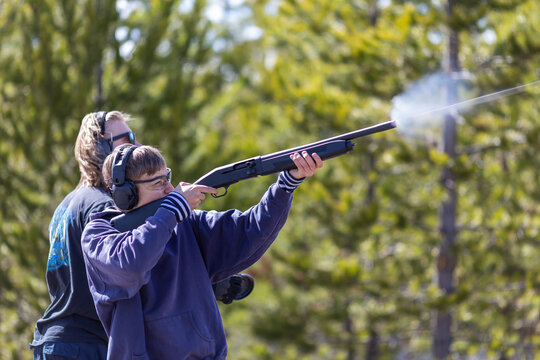 Two young man shooting shotgun. Shooting clay targets. Side view. Bullet trace. Gun powder gases from muzzle.