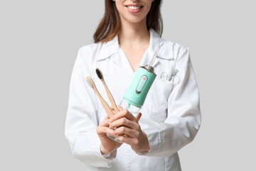 Female dentist with oral irrigator and toothbrushes on grey background
