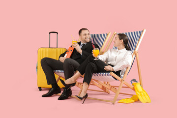 Happy office workers with cocktails sitting on deckchairs near suitcase on pink background. Summer...
