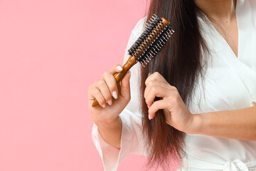 Beautiful young Asian woman brushing her hair on pink background, closeup