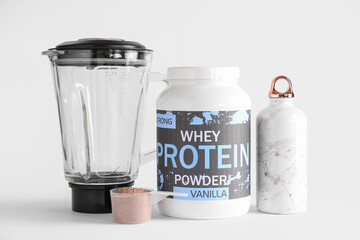 Bottle of protein powder, water and blender on light background
