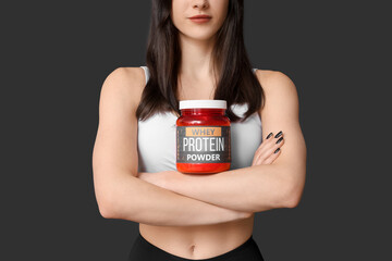 Beautiful sporty woman with bottle of protein powder on dark background