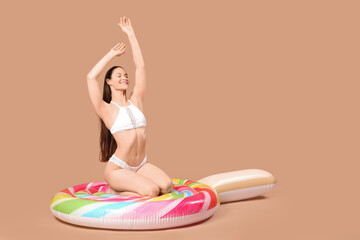 Woman in swimsuit sitting on inflatable mattress against brown background