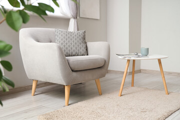 Interior of light living room with grey armchair and table