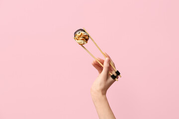 Hand with tasty sushi roll and chopsticks on pink background