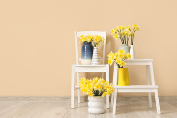 Composition with chair and vases of yellow narcissus flowers near beige wall in room