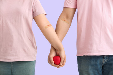 Blood donors with applied medical patches holding heart on lilac background, closeup