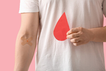 Blood donor with applied medical patches and paper blood drop on pink background, closeup