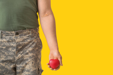 Soldier with applied medical patch and heart on yellow background. Blood donation concept