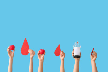 Female hands holding blood pack, test tube, hearts and paper blood drops on blue background. Blood...